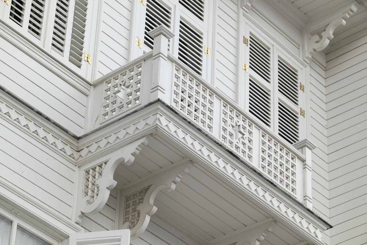Primer plano de un detallado balcón de madera blanca, característico de la arquitectura de las casas de verano en Büyükada, una de las Islas de los Príncipes. La imagen captura la carpintería fina y los celosías ornamentales, evocando el encanto nostálgico de este destino turco, emblemático de la vida 'Más Allá del Asfalto'.