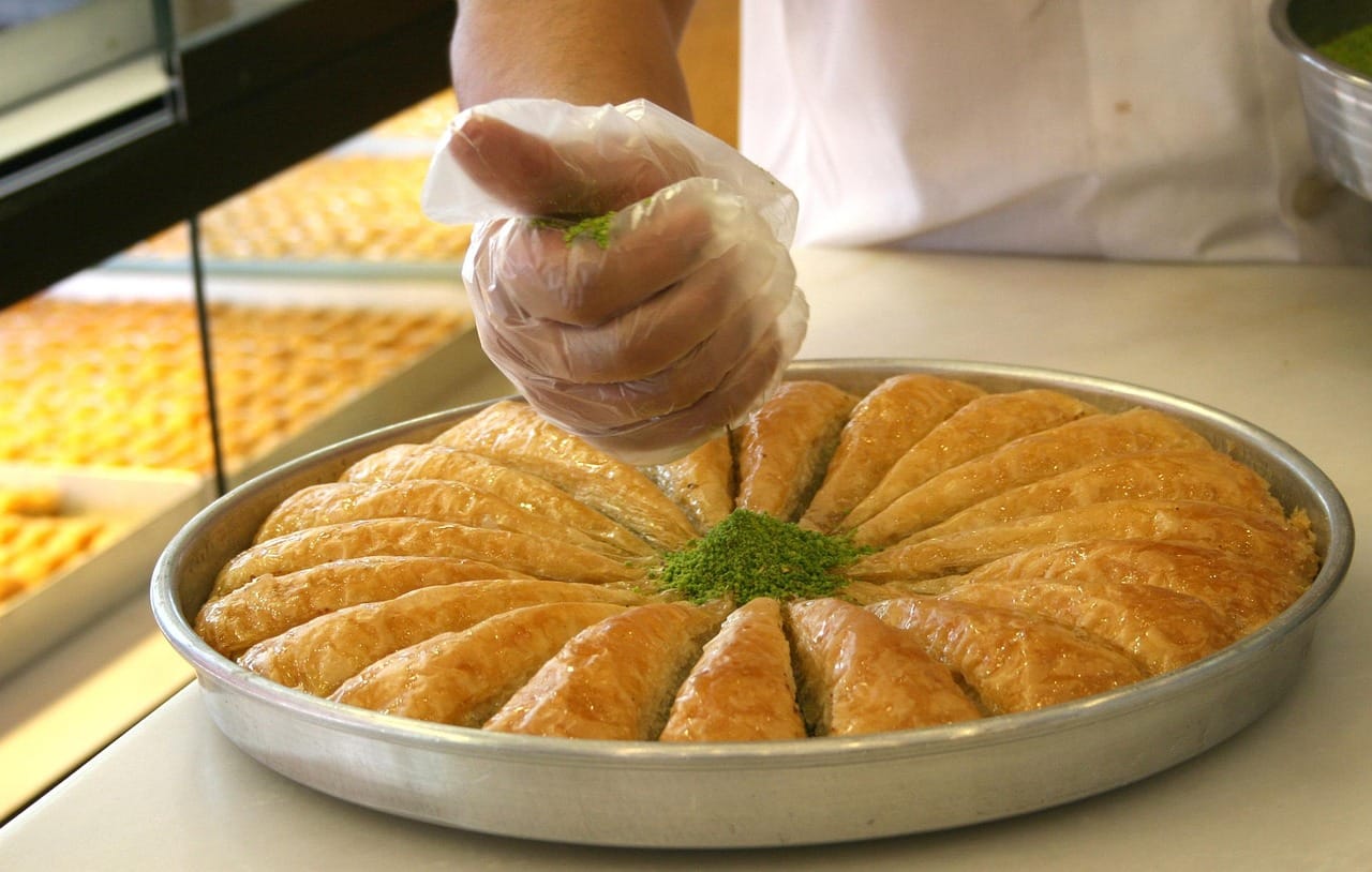 Pastelero añadiendo pistacho picado a una bandeja redonda de baklava recién horneado.