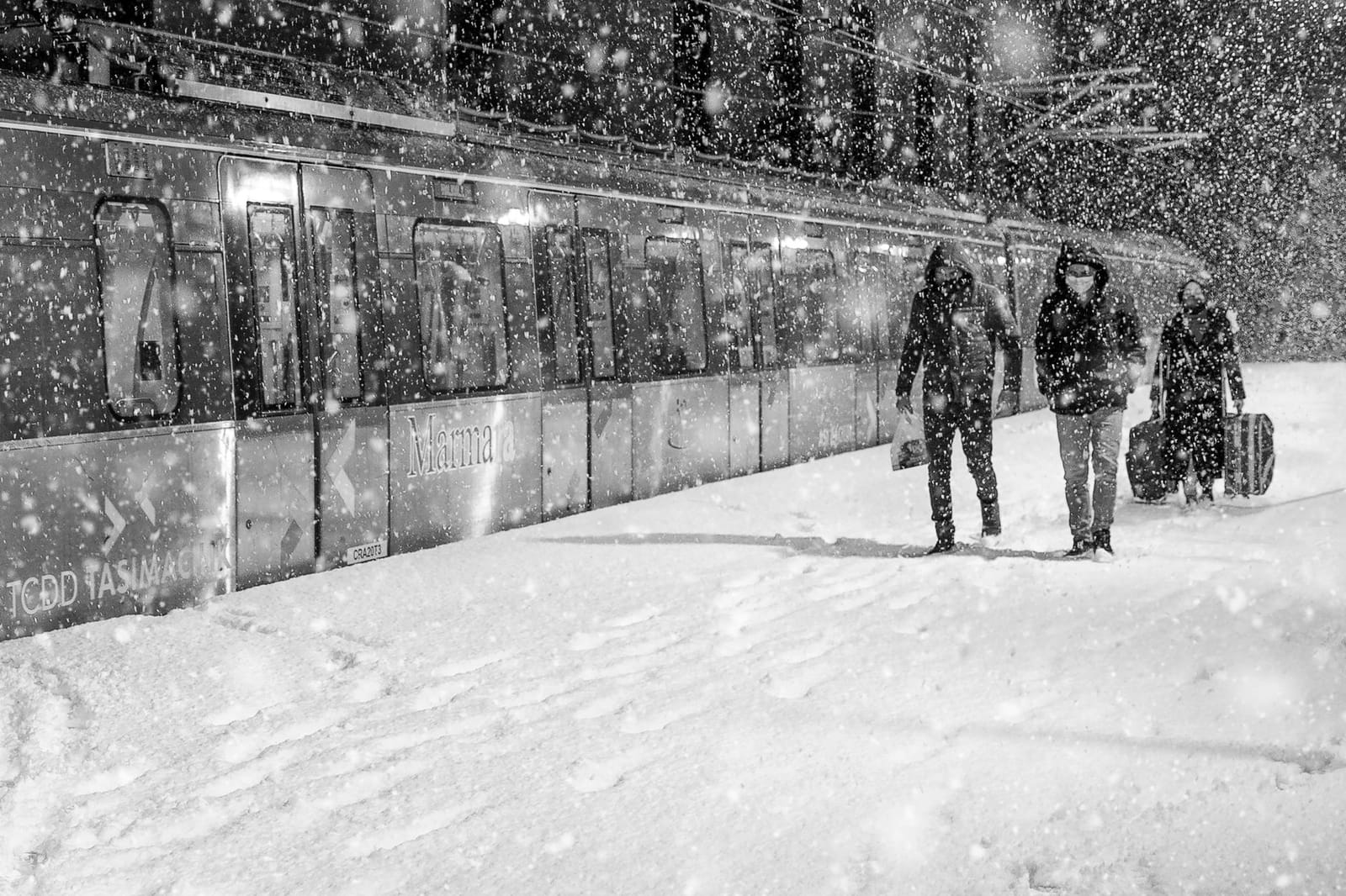 Pasajeros caminando junto a un tren Marmaray en un andén cubierto de nieve.
