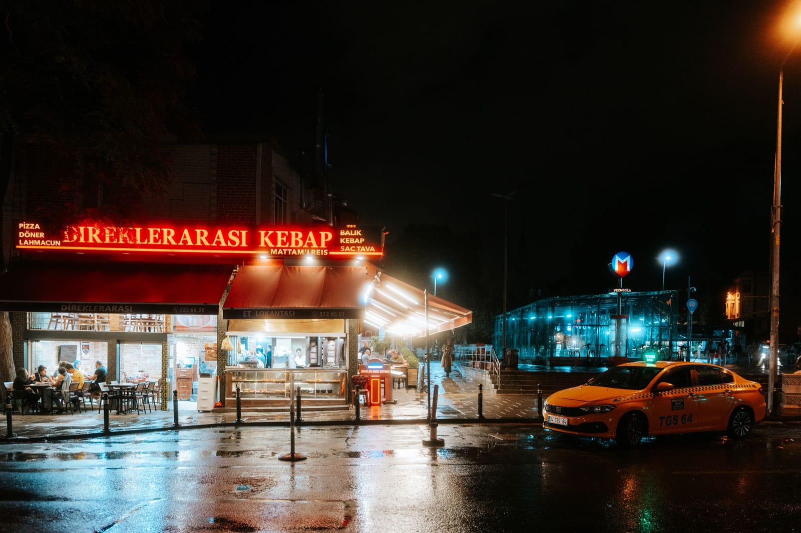 Entrada iluminada de metro y taxi tradicional en una calle nocturna de Estambul.