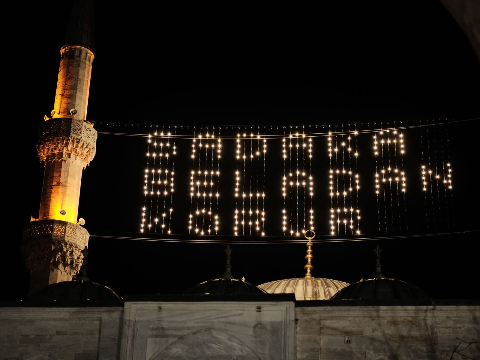 Luces tradicionales mahya colgadas entre minaretes de una mezquita durante Ramadán.