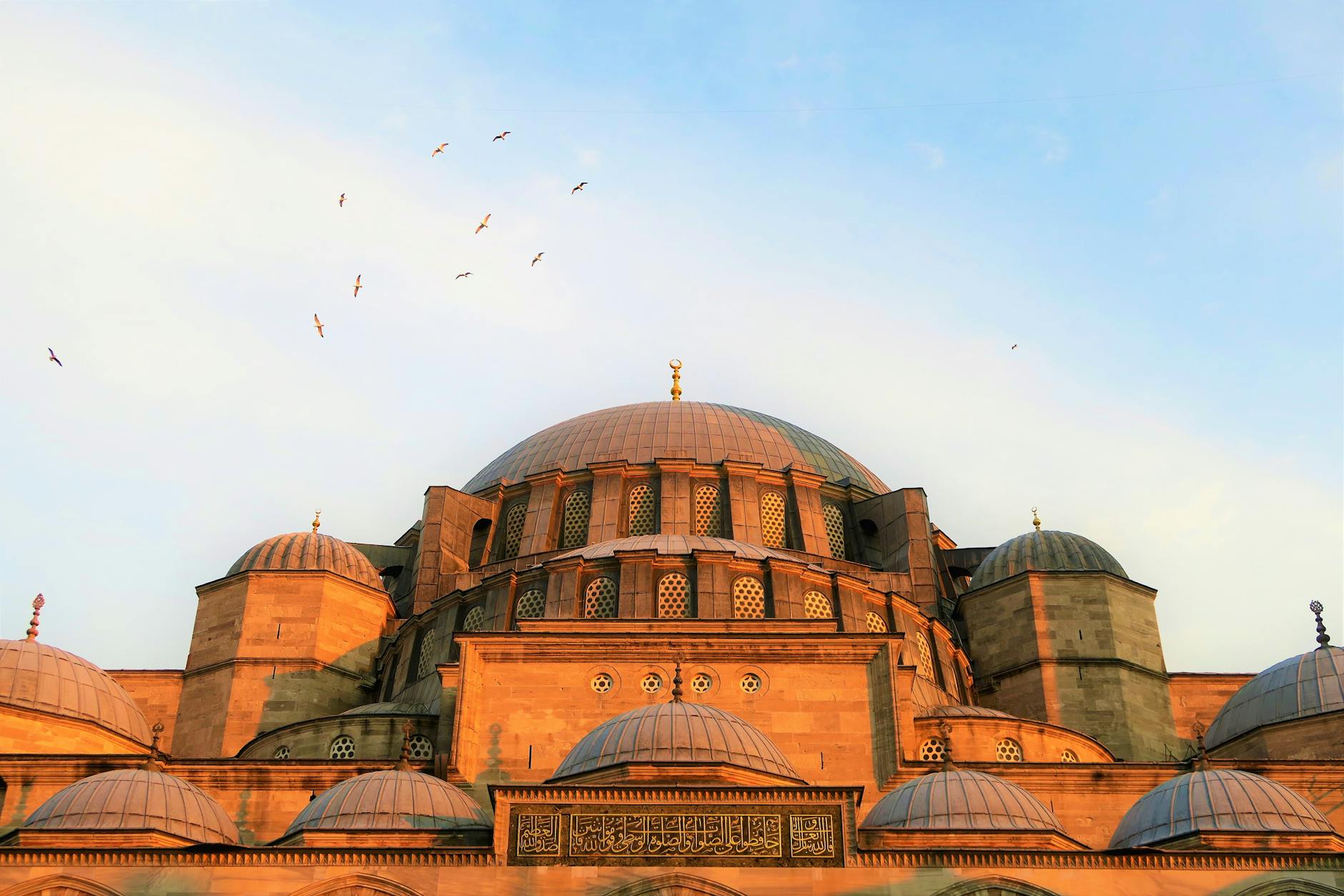 Cúpulas y detalles arquitectónicos de la Mezquita de Süleymaniye iluminados por la luz del atardecer, con pájaros volando en el cielo azul claro de Estambul.
