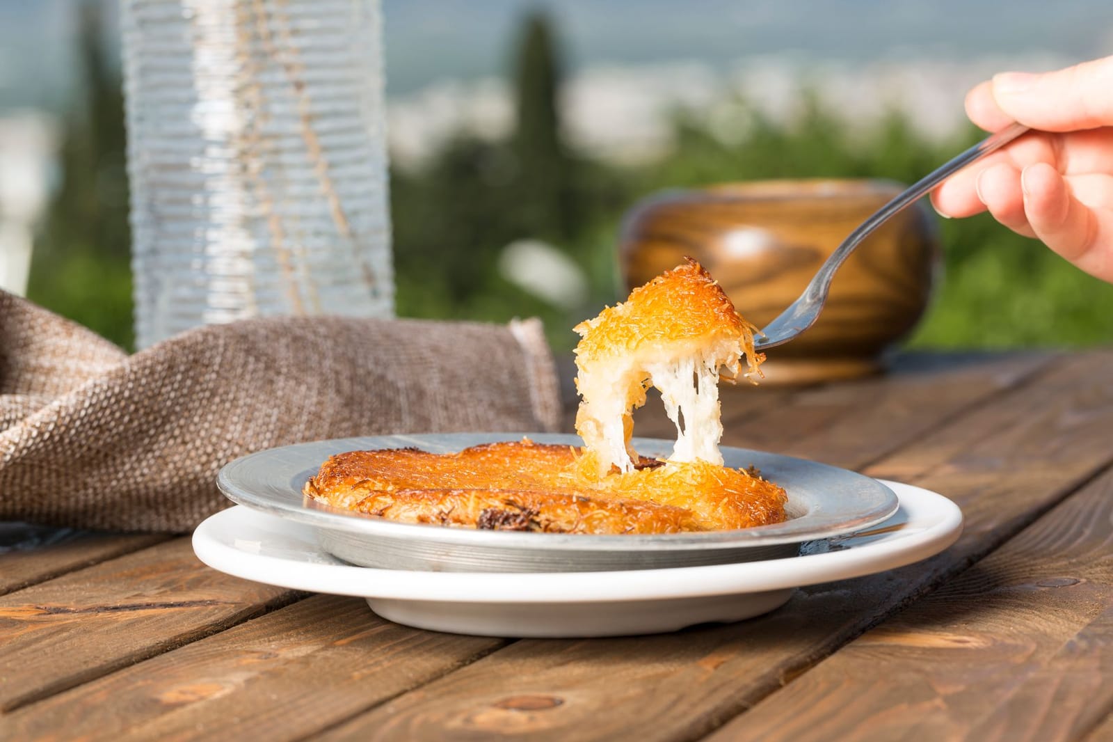 Porción de künefe tradicional turco con queso fundido servido al aire libre.