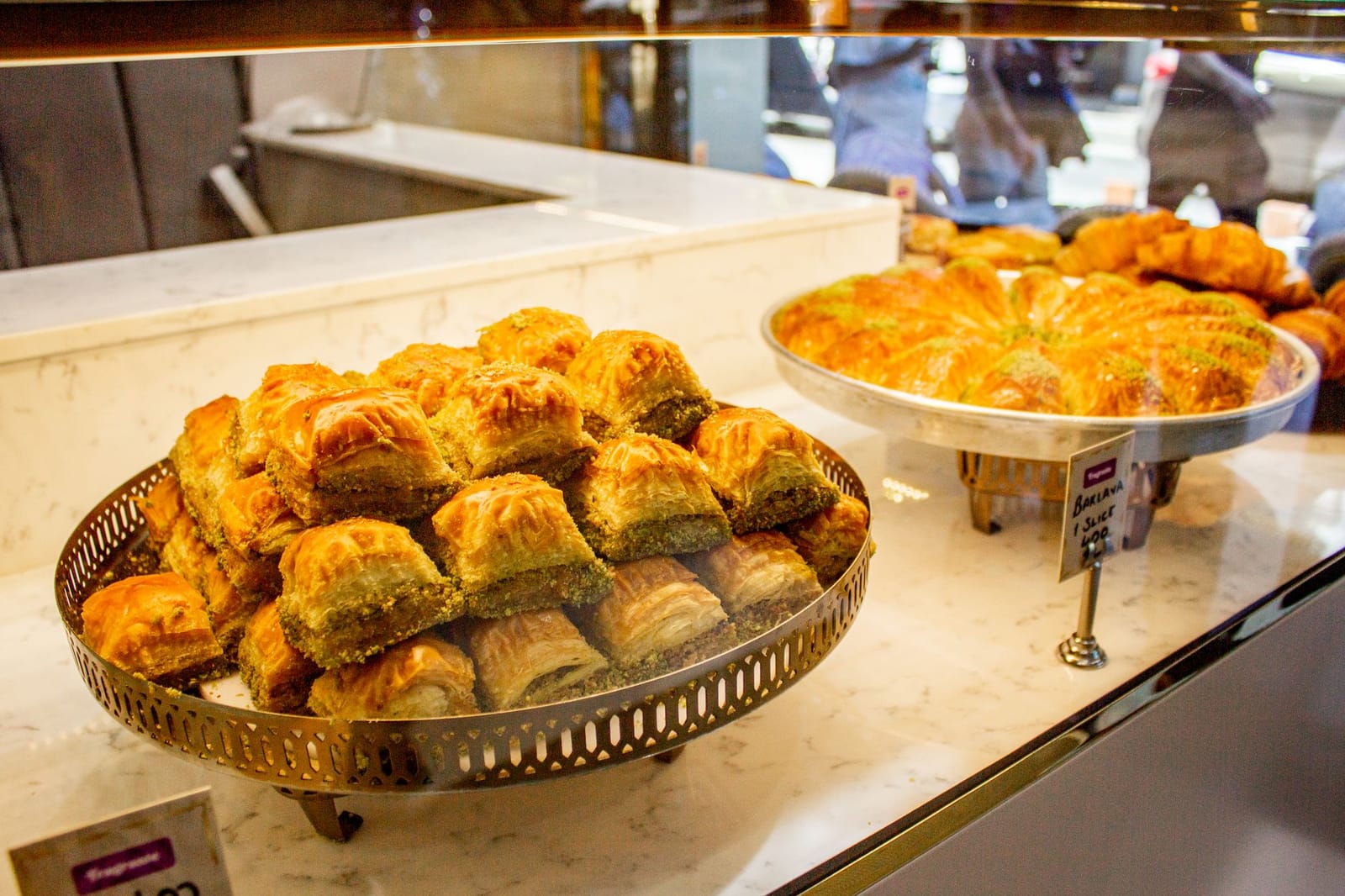 Porciones de baklava tradicional turco exhibidas con precios en una pastelería.