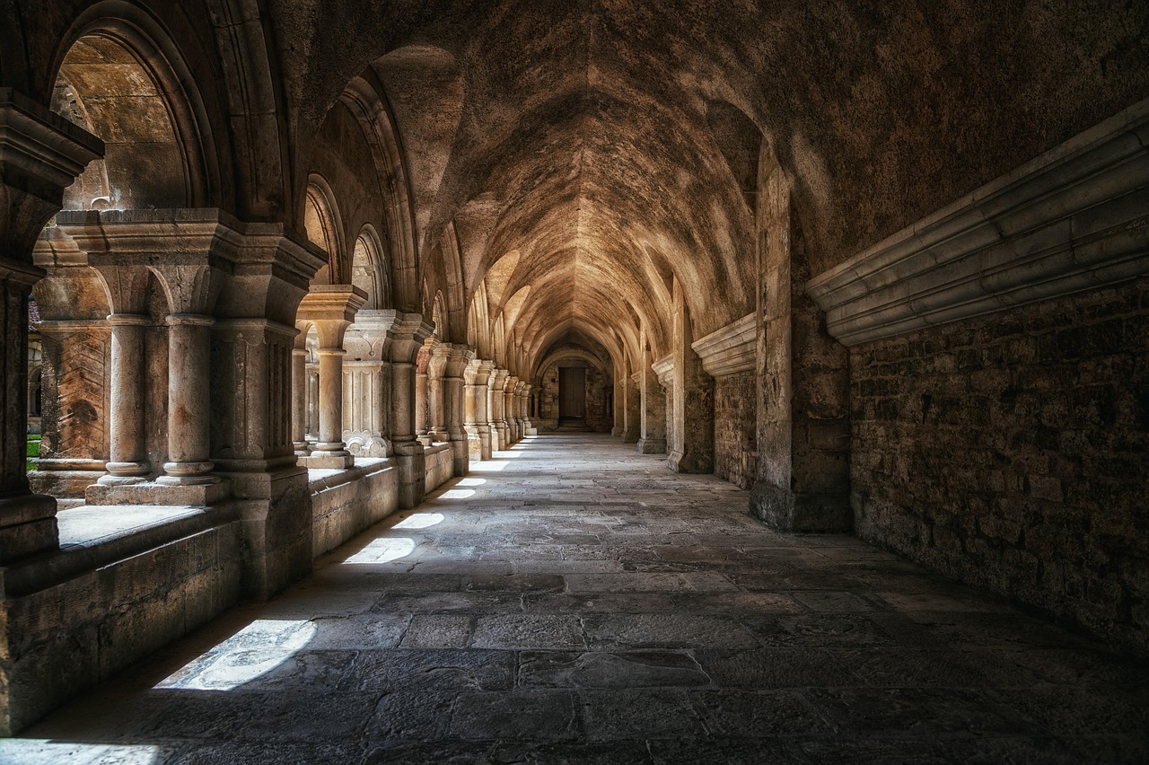 Pasillo abovedado y oscuro con columnas de piedra iluminado por la luz que entra desde la izquierda, evocando la arquitectura del Monasterio de Cristo Pantócrator en Zeyrek, Estambul.